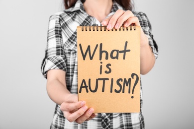 Photo of Woman holding notebook with words WHAT IS AUTISM on light background
