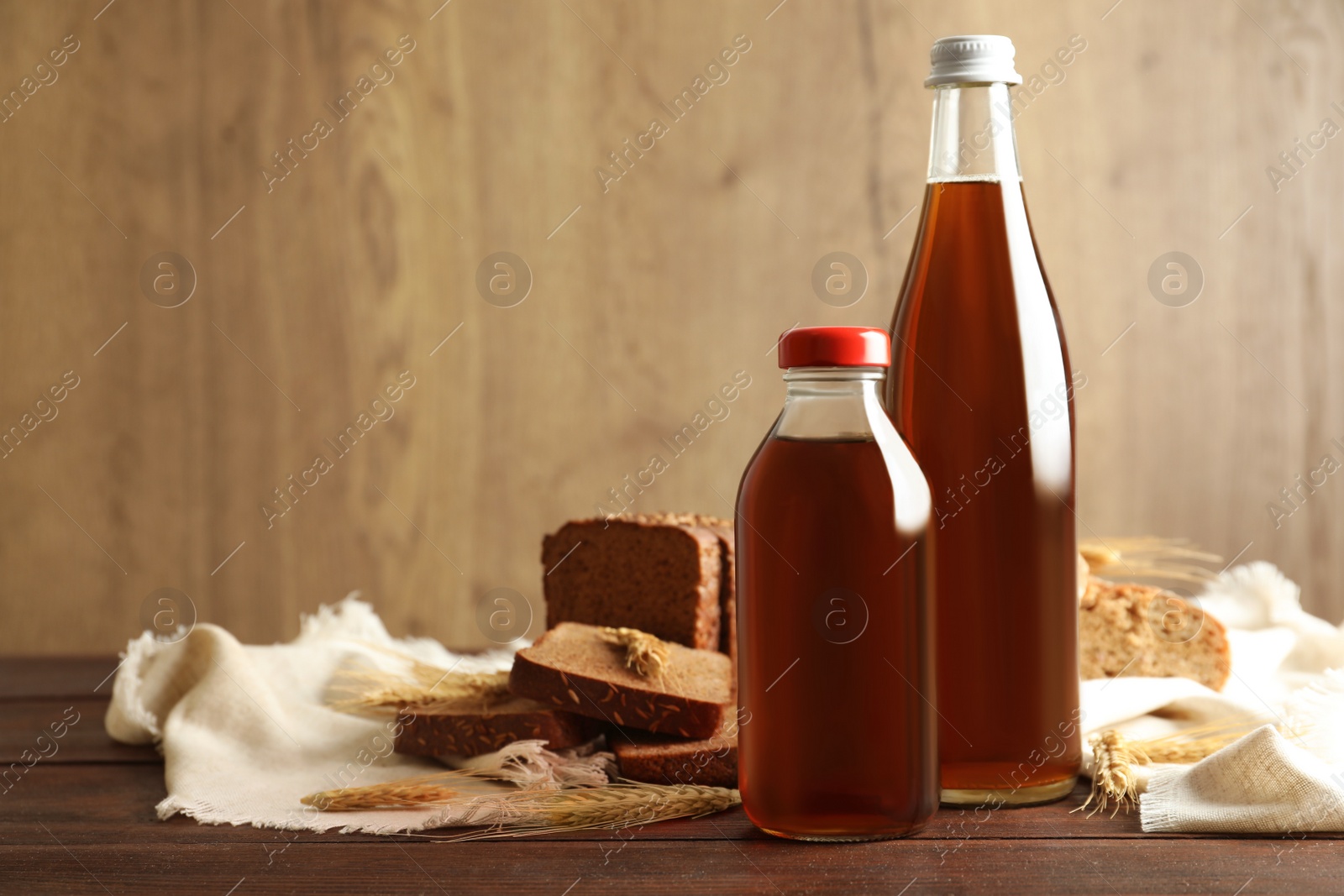 Photo of Bottles of delicious fresh kvass, spikelets and bread on wooden table