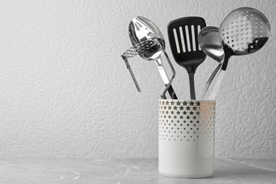 Photo of Set of kitchen utensils in stand on stone table near light wall. Space for text