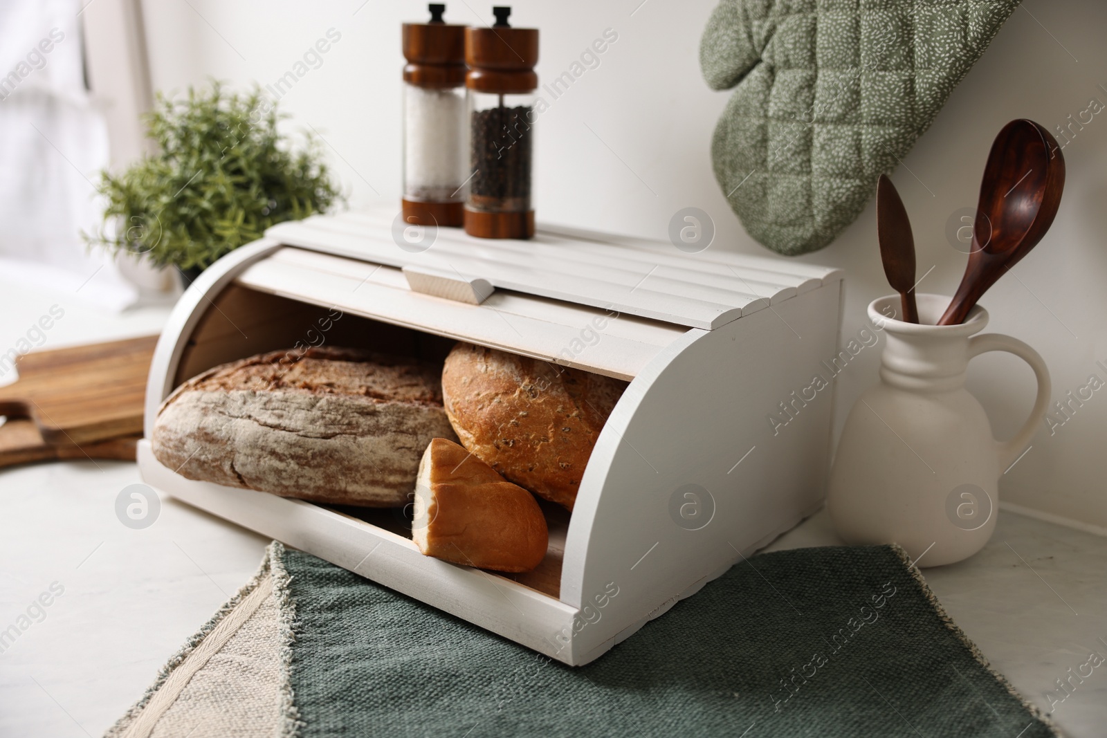 Photo of Wooden bread basket with freshly baked loaves on white marble table in kitchen