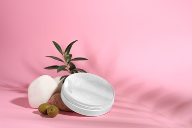 Photo of Jar of natural cream, stones and olives on pink background, space for text. Cosmetic products