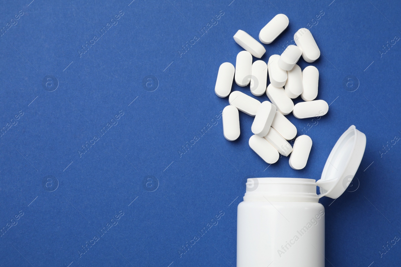 Photo of Vitamin pills and bottle on blue background, top view. Space for text