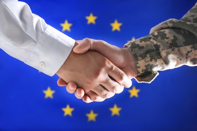 Photo of Soldier and businessman shaking hands against flag of European Union, closeup