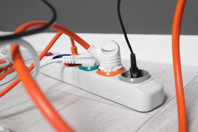 Photo of Power strip with different electrical plugs on white laminated floor indoors, closeup