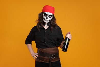 Man in scary pirate costume with skull makeup and bottle of rum on orange background. Halloween celebration