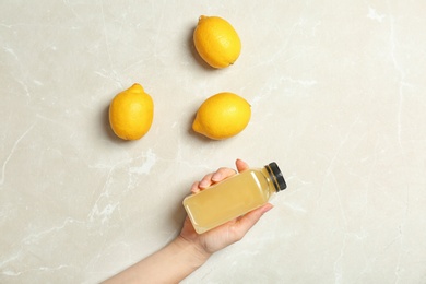 Photo of Woman holding bottle with fresh juice near lemons on light background, top view