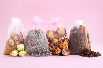Photo of Scented sachets with dried flowers, coffee beans and spices on pink background