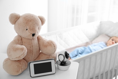 Photo of Baby monitor, camera and toy on table near crib with child in room. Video nanny