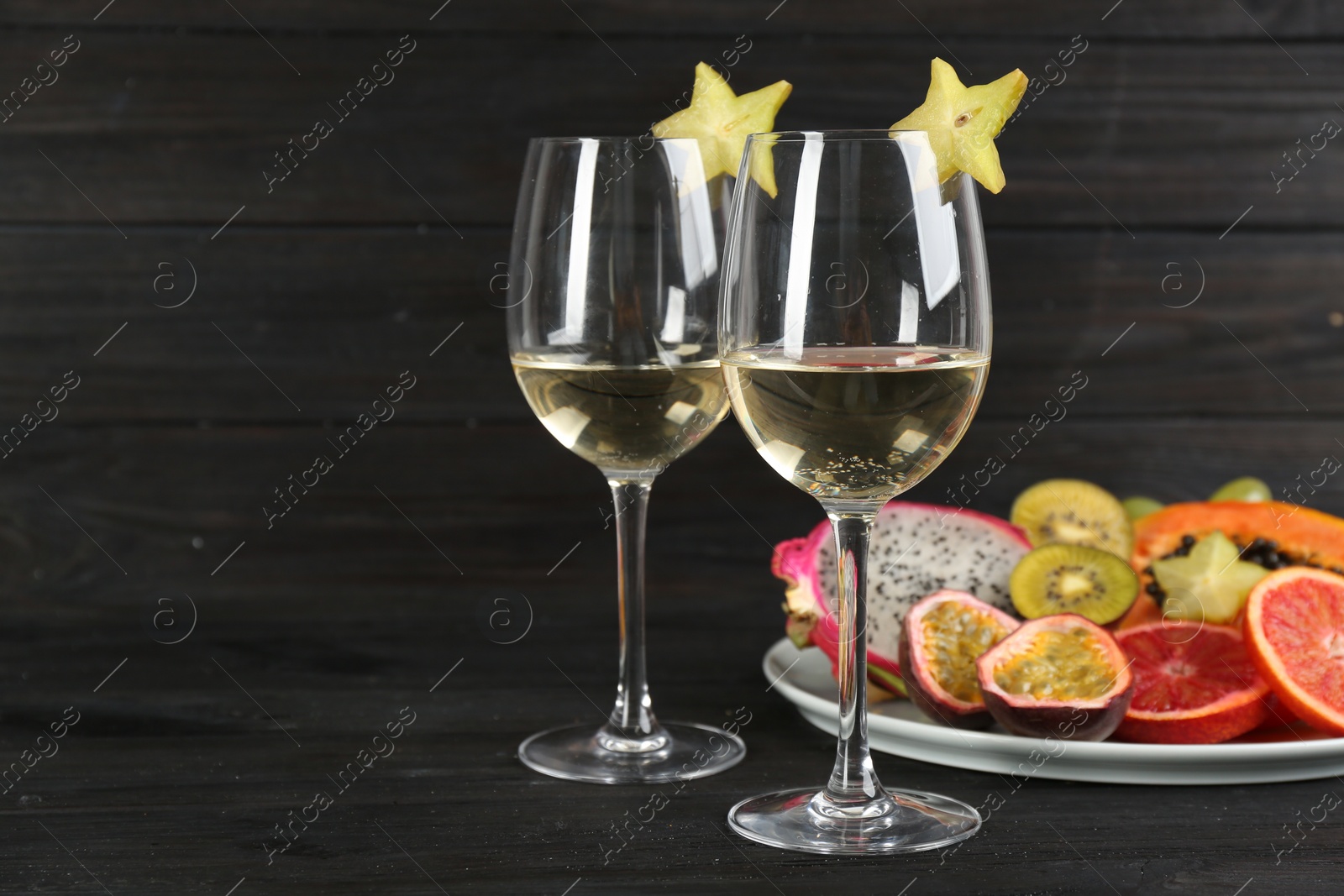 Photo of Delicious exotic fruits and wine on black wooden table. Space for text
