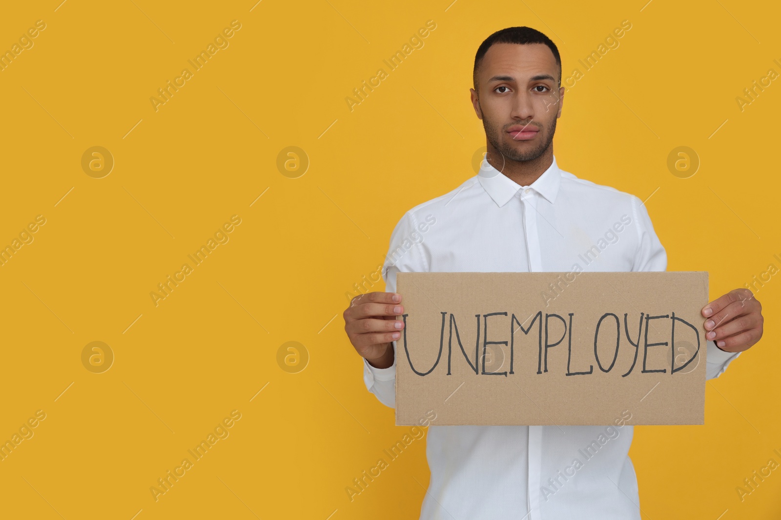 Photo of Young man holding sign with word Unemployed on yellow background. Space for text