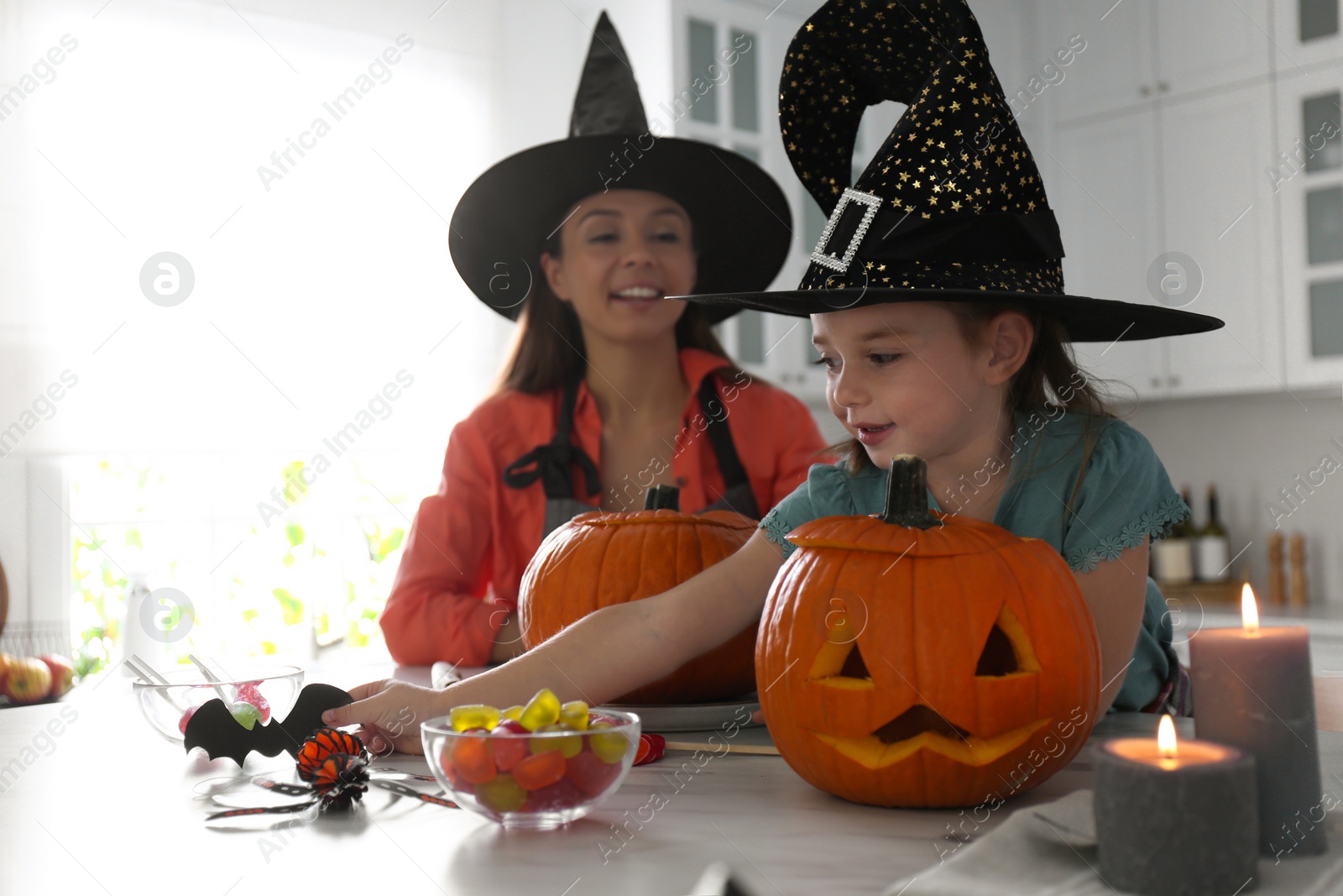 Photo of Mother and daughter making pumpkin jack o'lanterns at table in kitchen. Halloween celebration