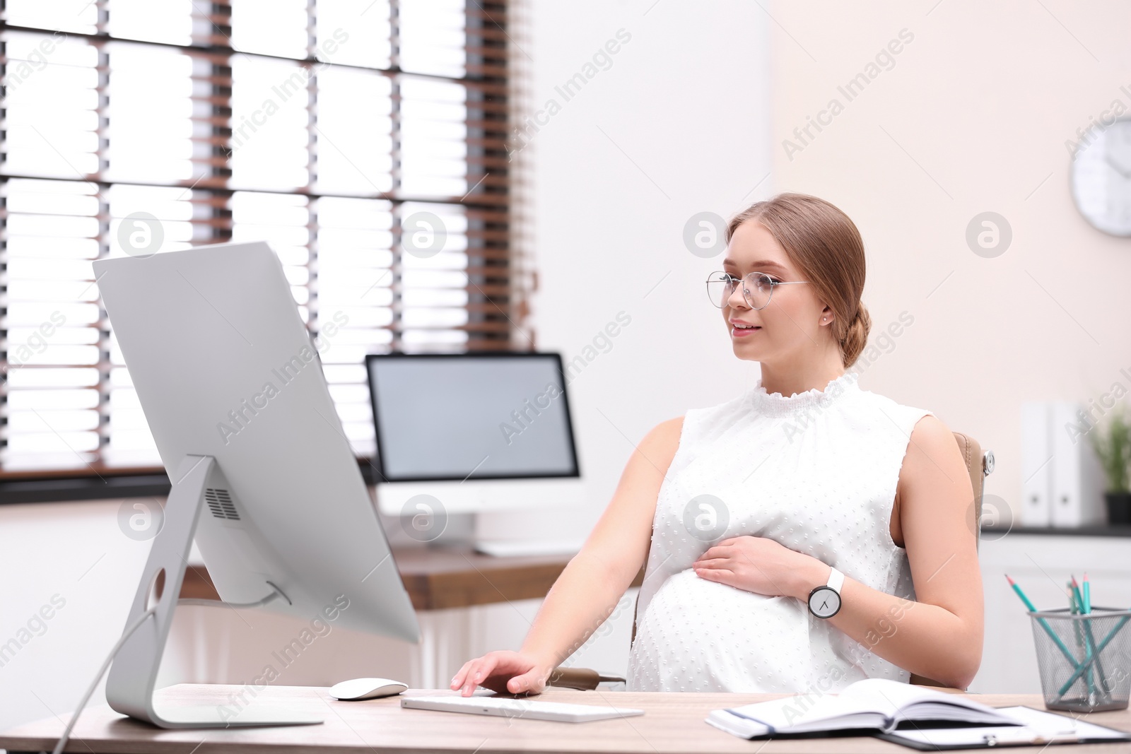 Photo of Young pregnant woman working with computer at table in office