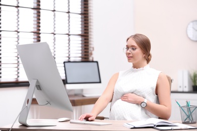 Young pregnant woman working with computer at table in office