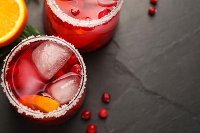 Photo of Tasty cranberry cocktail with ice cubes in glasses on dark gray textured table, flat lay. Space for text