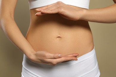 Photo of Woman holding hands near belly against beige background, closeup
