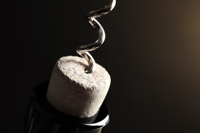 Photo of Opening bottle of wine with corkscrew on dark background, closeup