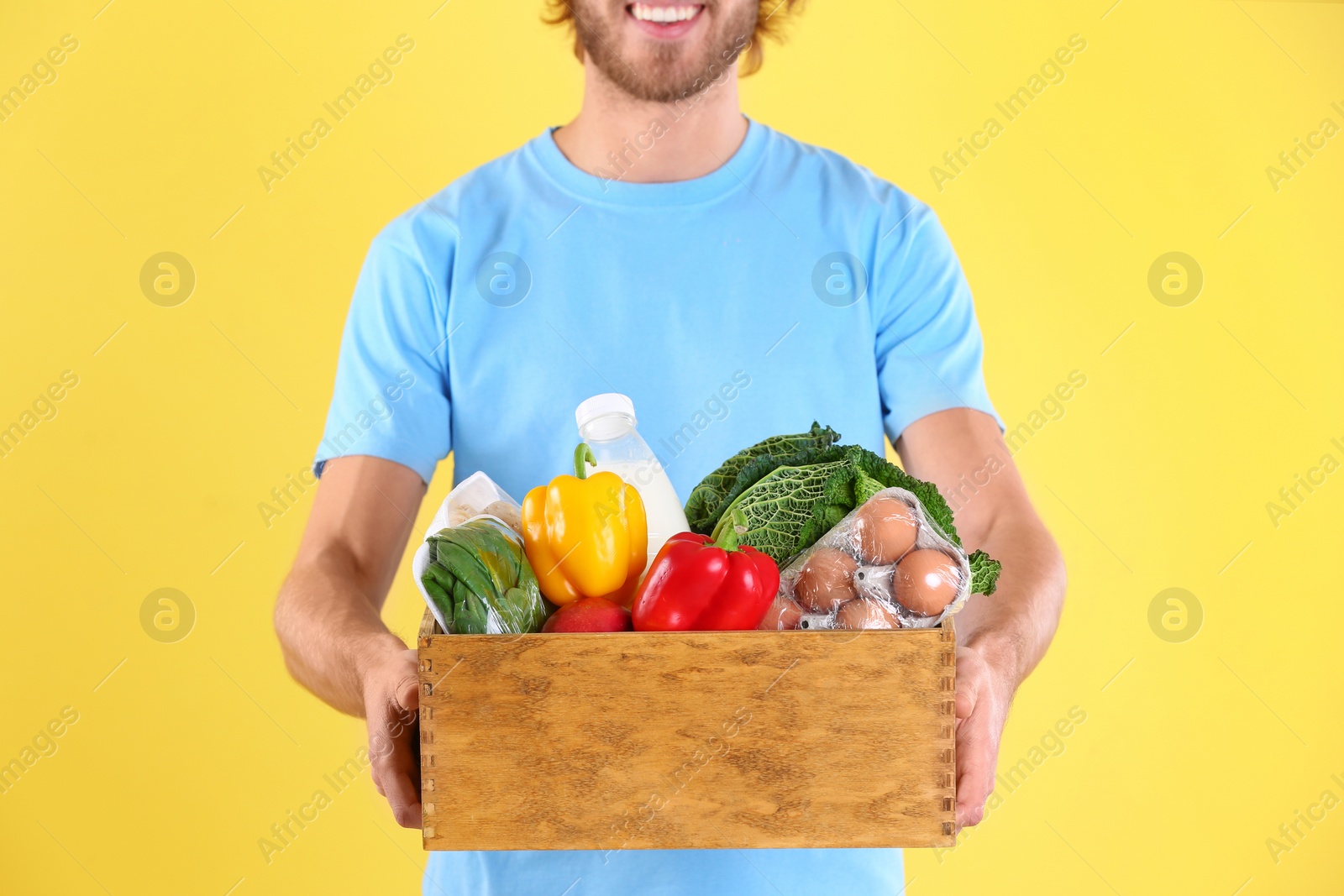 Photo of Delivery man holding wooden crate with food products on color background, closeup