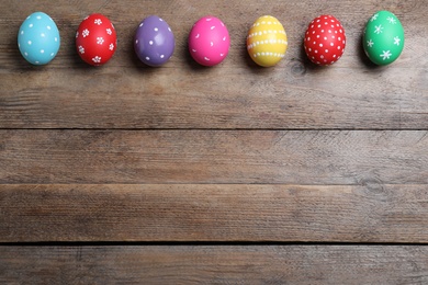Colorful eggs on wooden background, flat lay with space for text. Happy Easter