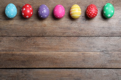 Photo of Colorful eggs on wooden background, flat lay with space for text. Happy Easter