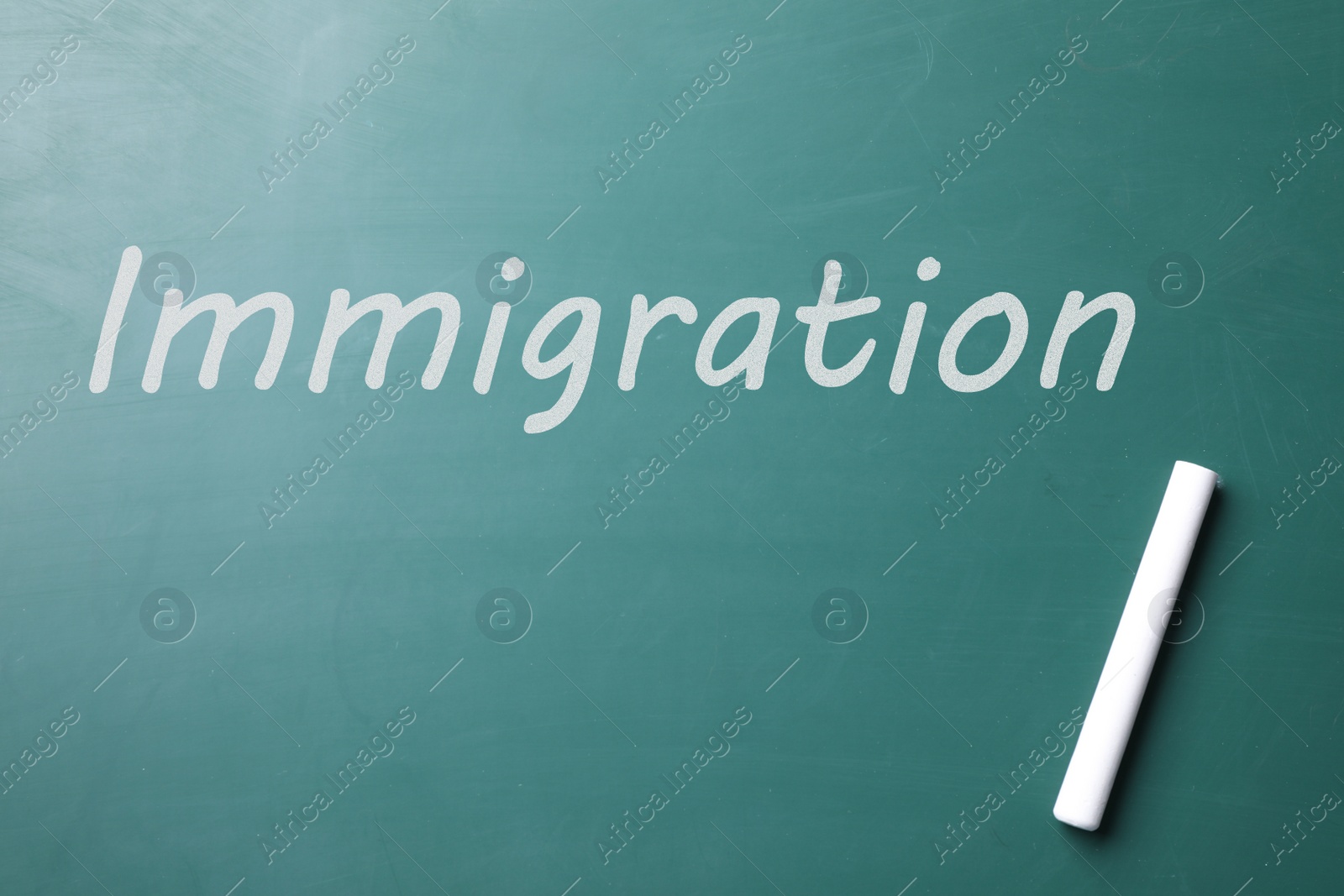 Image of Piece of white chalk and word IMMIGRATION written on greenboard, top view