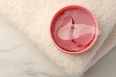 Photo of Jar of under eye patches with spoon and towel on white marble table, top view. Care products