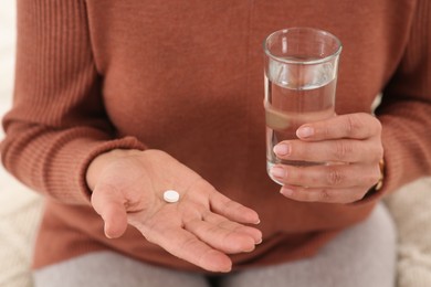 Senior woman with pill and glass of water indoors, closeup