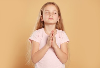 Photo of Girl with clasped hands praying on beige background
