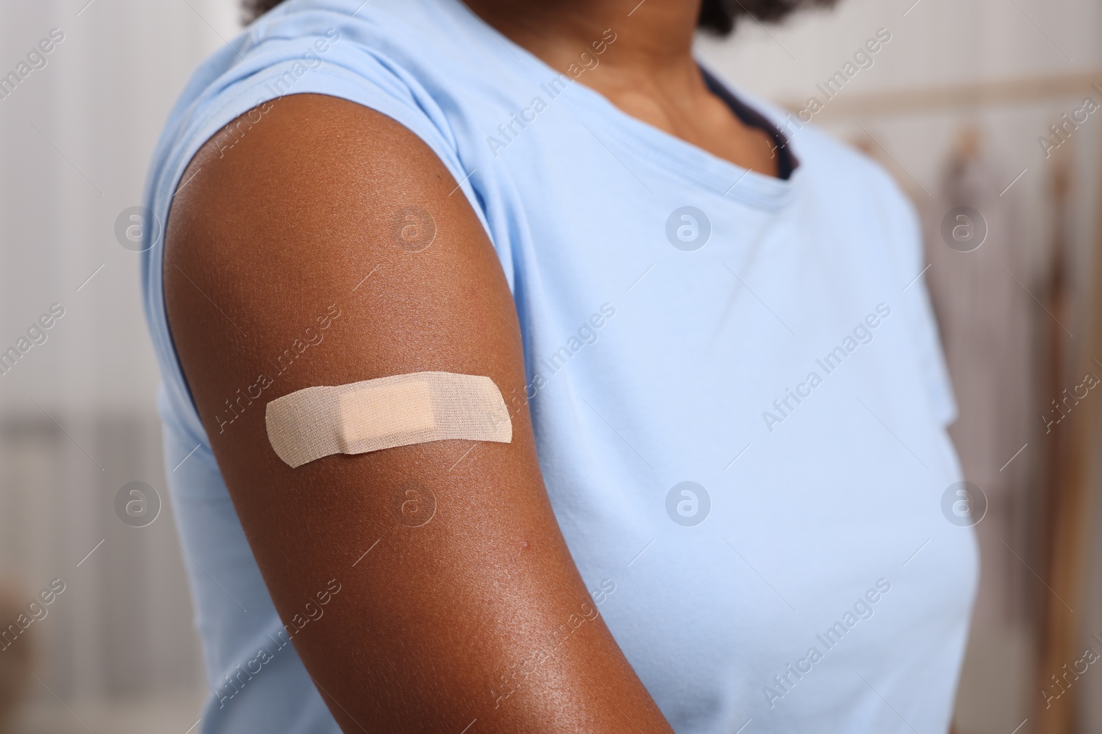 Photo of Young woman with adhesive bandage on her arm after vaccination indoors, closeup