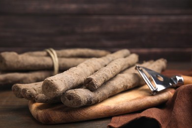 Photo of Raw salsify roots and peeler on wooden table, closeup
