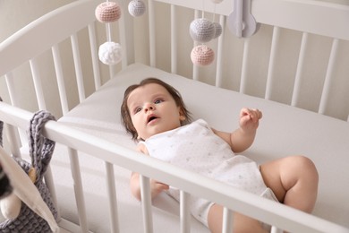 Photo of Cute little baby looking at hanging mobile in crib