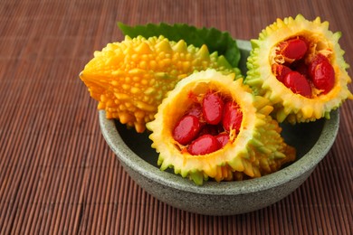 Many fresh bitter melons in bowl on bamboo mat, closeup