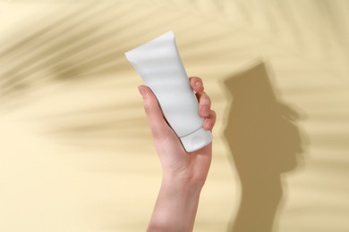 Photo of Woman holding tube of cream on yellow background, closeup