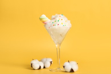 Photo of Martini glass with cotton, sprinkles and marshmallow on yellow background
