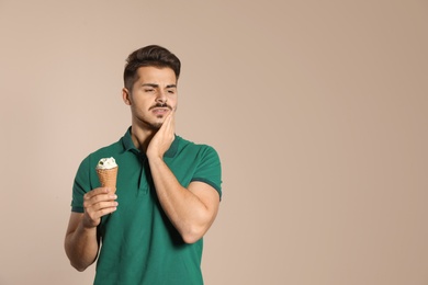 Emotional young man with sensitive teeth and ice cream on color background. Space for text