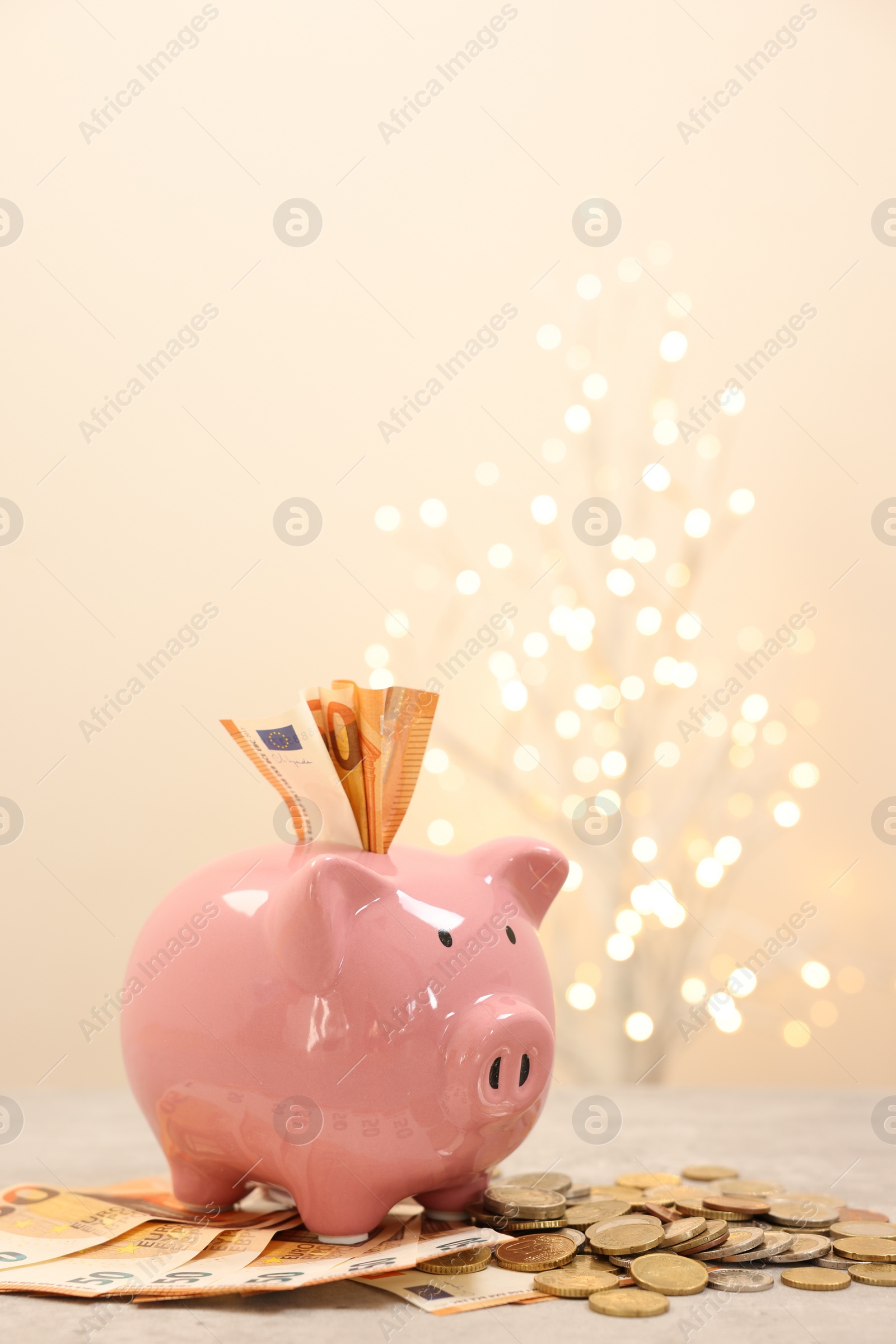 Photo of Piggy bank with euro banknotes and coins on grey table against blurred lights, space for text