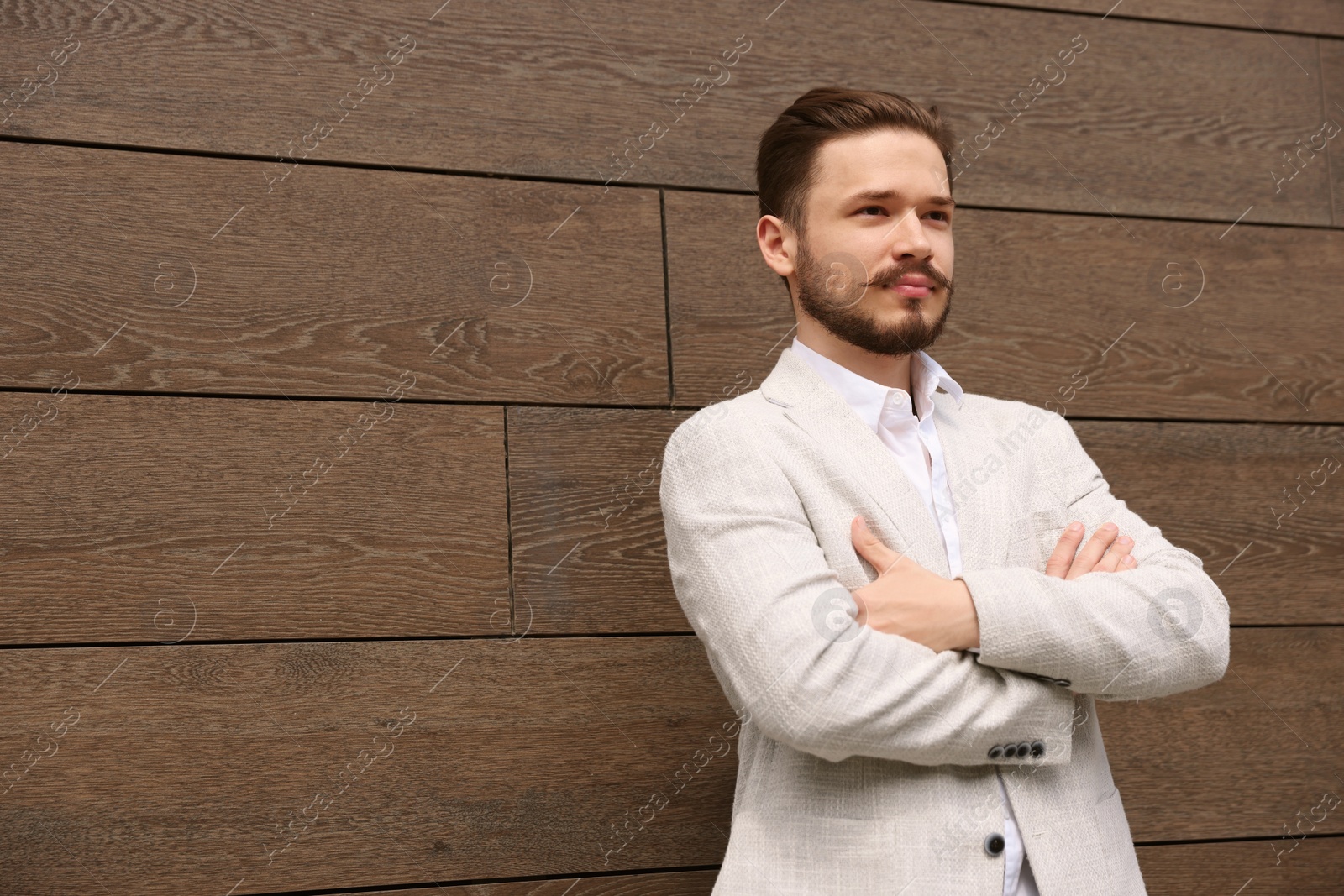 Photo of Smiling man in white suit crossing his arms near brown brick wall. Space for text