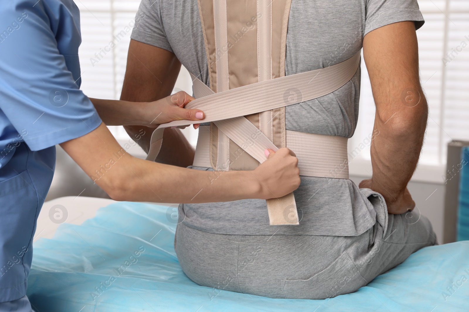 Photo of Orthopedist helping patient to put on posture corrector in clinic, closeup. Scoliosis treatment