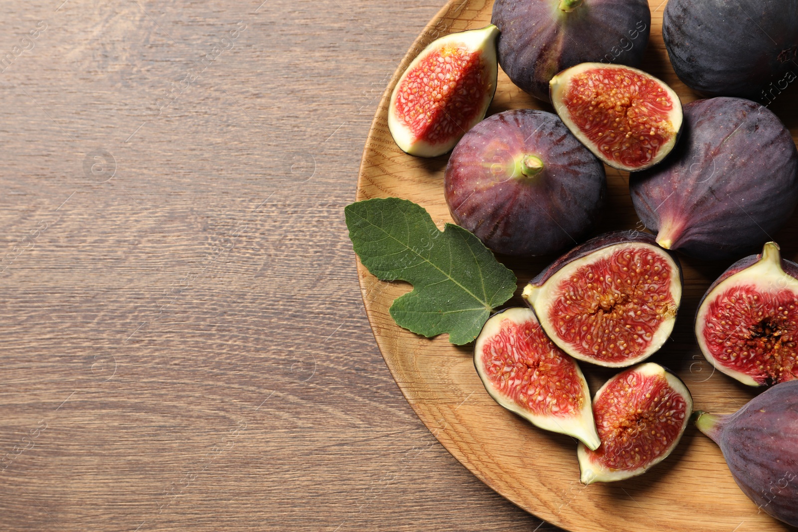 Photo of Whole and cut ripe figs with leaf on wooden table, top view. Space for text