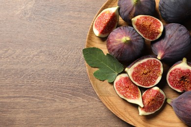 Whole and cut ripe figs with leaf on wooden table, top view. Space for text