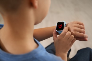 Image of Little boy using SOS function on smartwatch indoors, closeup