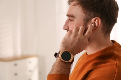 Photo of Young man with smart watch and earphones at home, space for text