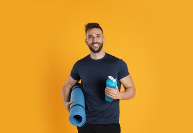 Handsome man with yoga mat and shaker on yellow background