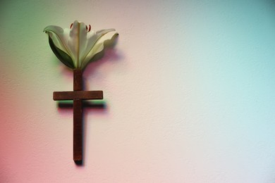 Photo of Wooden cross and lily flower on textured table in color lights, top view with space for text. Religion of Christianity
