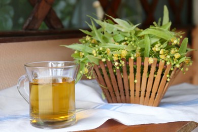 Photo of Glass cup of aromatic tea and linden blossoms on wooden table