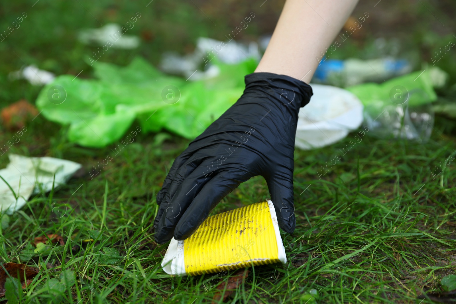 Photo of Woman collecting garbage on green grass, closeup