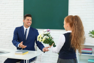 Photo of Schoolgirl congratulating her pedagogue with bouquet in classroom. Teacher's day