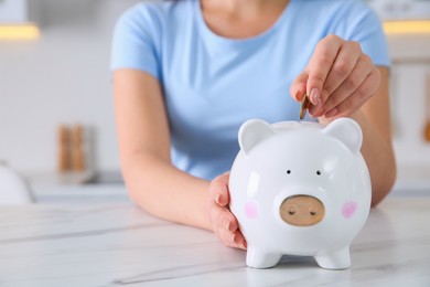 Photo of Young woman putting coin into piggy bank at table indoors, closeup and space for text. Money savings