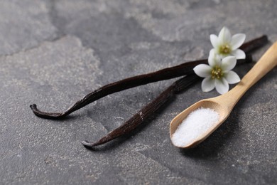 Photo of Spoon with sugar, flowers and vanilla pods on grey textured table, closeup