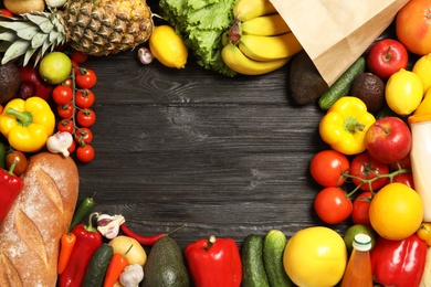 Photo of Frame with shopping paper bag and different groceries on dark wooden background, flat lay. Space for text