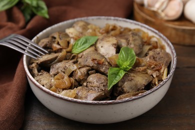 Photo of Delicious fried chicken liver with onion and basil in bowl on wooden table, closeup